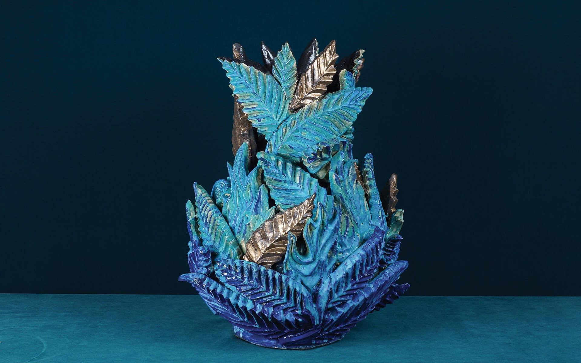 Intricate ceramic sculpture with blue and teal leaf designs against a dark blue background.