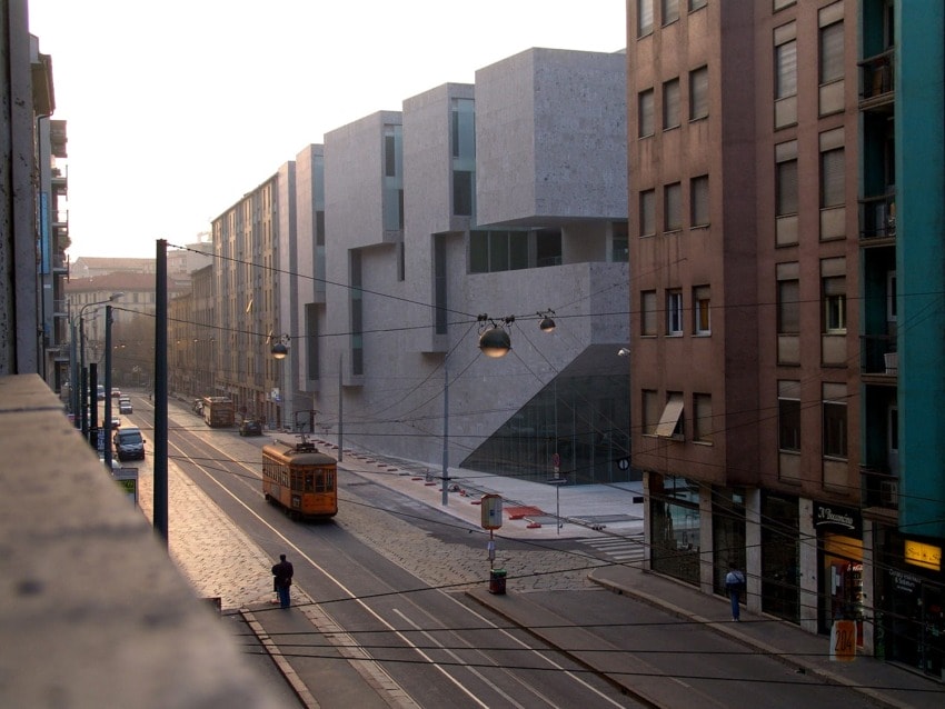 Street scene with an orange tram traveling through a city’s urban landscape at sunrise, surrounded by modern and classic buildings.