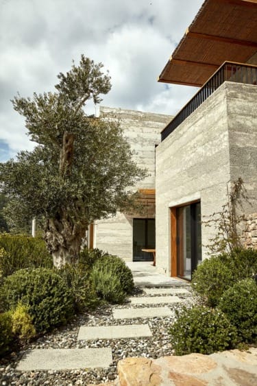 Modern house with stone facade and wooden accents surrounded by greenery and cloudy sky in the background