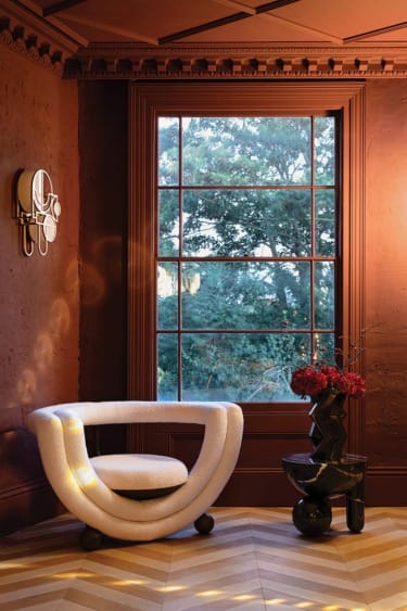 Modern room with a round white chair, art deco side table, red flowers, and a large window overlooking trees.