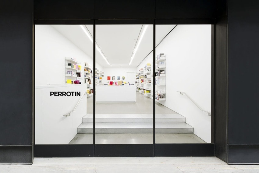Storefront entrance of a modern art gallery with white interior and shelves displaying books and art pieces.