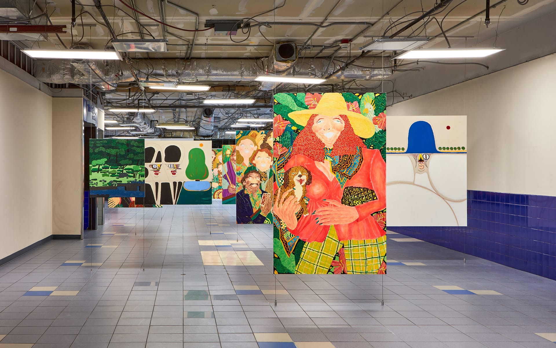 Colorful paintings displayed in an industrial-style hallway with tile flooring and exposed ceiling fixtures.