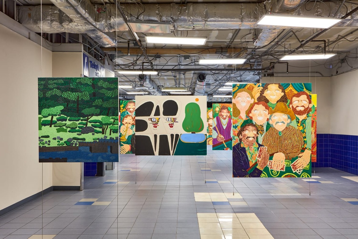 Art installations with vibrant colors and geometric patterns hanging in a tiled corridor with exposed ceiling pipes.