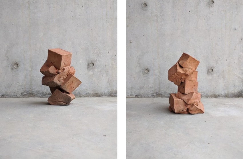 Stacked red bricks forming sculptures against a concrete wall in a minimalist art installation.