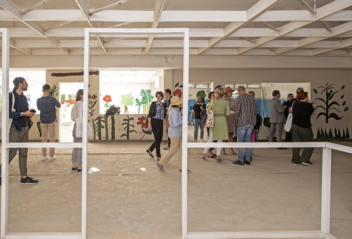 People viewing an art installation with paintings of flowers and plants in a bright, open gallery space.
