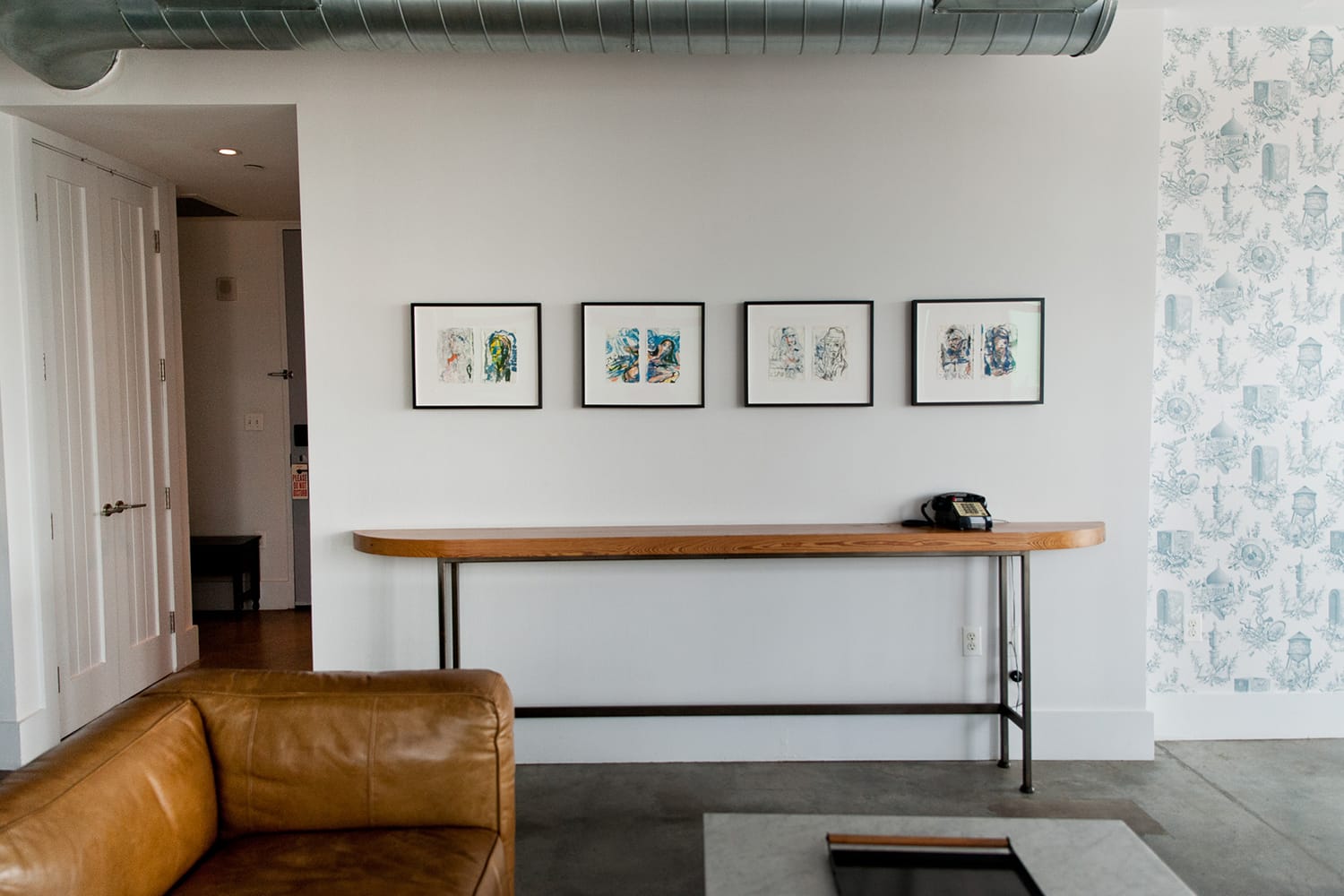 Modern living room with leather couch, framed artwork on white wall, vintage telephone on wooden console table.