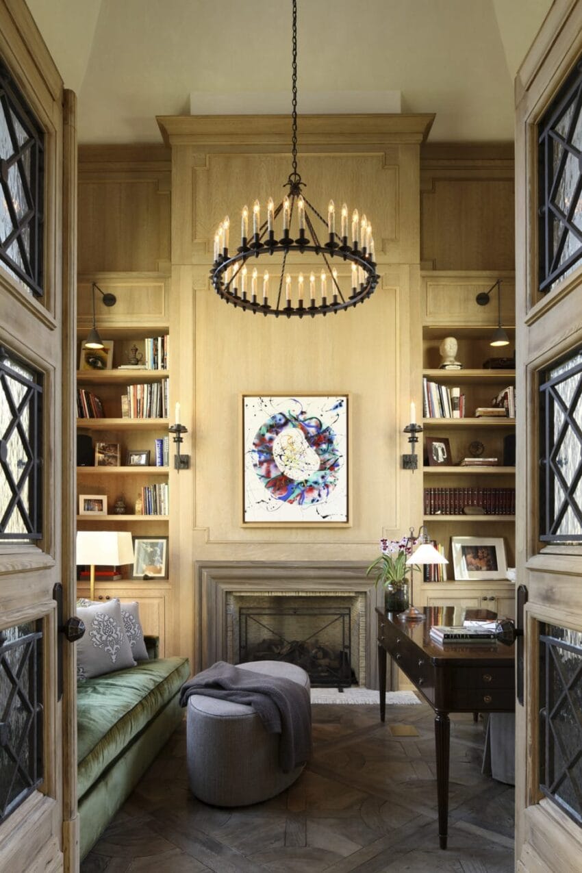 Elegant study with chandelier, fireplace, and wooden bookshelves; a green sofa and desk enhance the cozy ambiance.