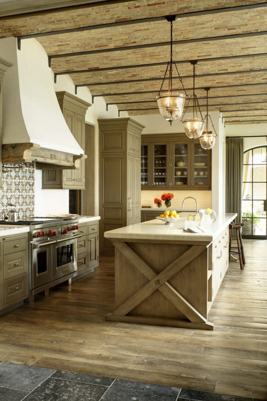 Rustic kitchen with wood cabinets, large island, hanging light fixtures, and brick ceiling.