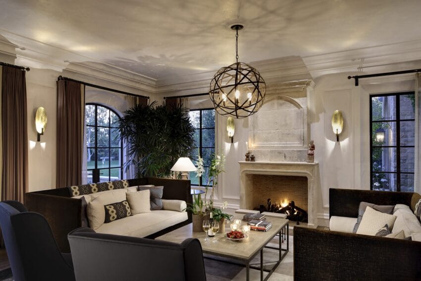 Elegant living room with modern chandelier, sofas, large windows, and a cozy fireplace surrounded by decor elements.