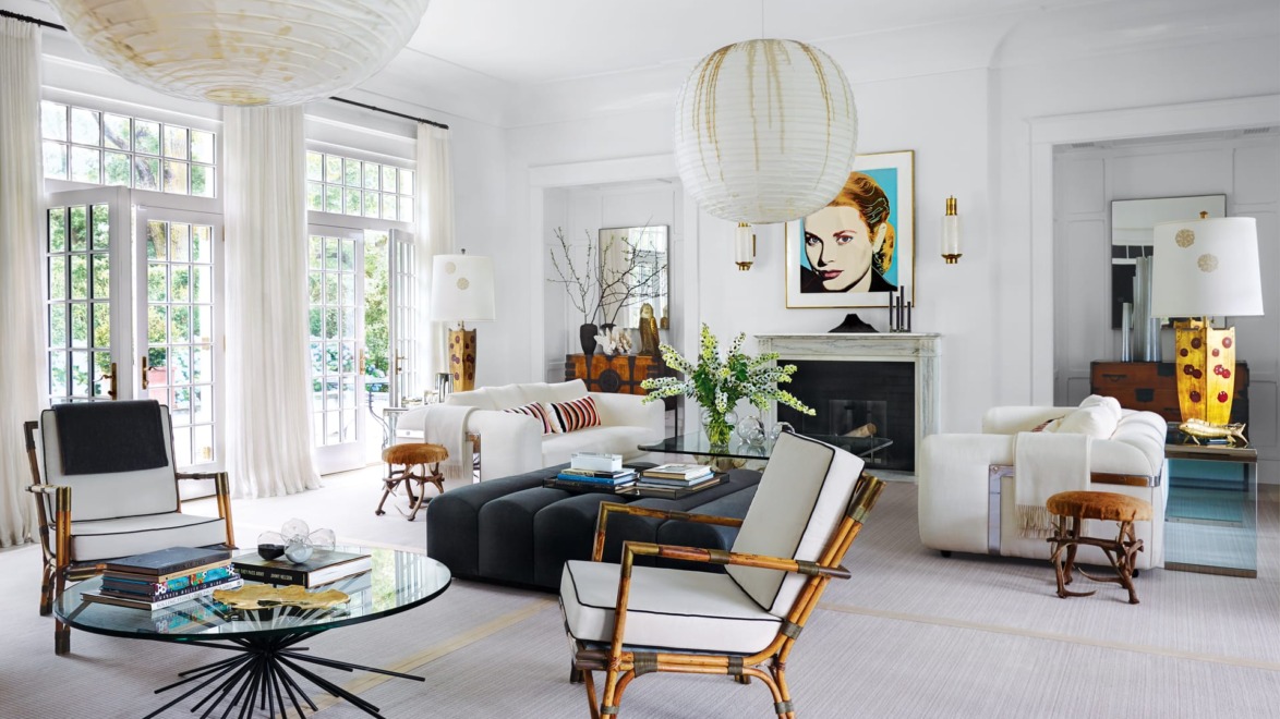Modern living room with large windows, white sofas, artistic decor, and a round glass coffee table on a light rug.