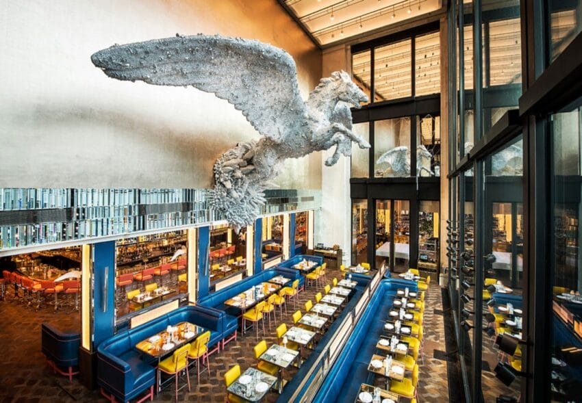 Modern restaurant interior with large Pegasus sculpture, colorful seating, and high ceilings.