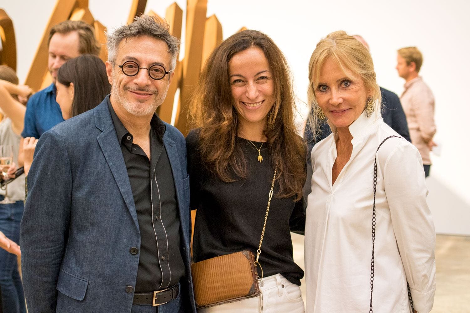 Three people smiling at an art gallery event with sculptural artwork in the background.
