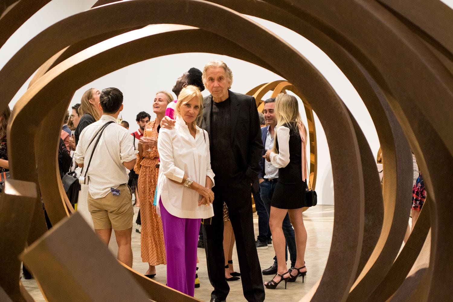 Guests mingling at an art gallery event, surrounded by large sculptural installations, engaging in conversation.