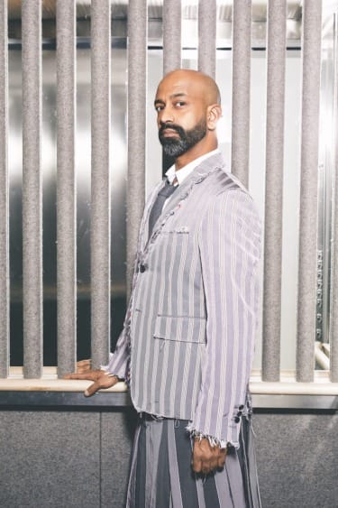 Man in striped suit standing in front of vertical slats.