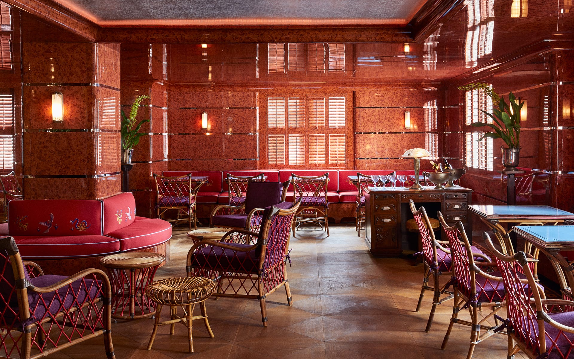 Art Deco style lounge with wicker furniture, red walls, round sofas, and warm lighting, creating a cozy atmosphere.