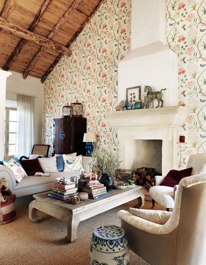 Rustic living room with floral wallpaper, wooden ceiling, stone fireplace, beige furniture, and decorative accessories.