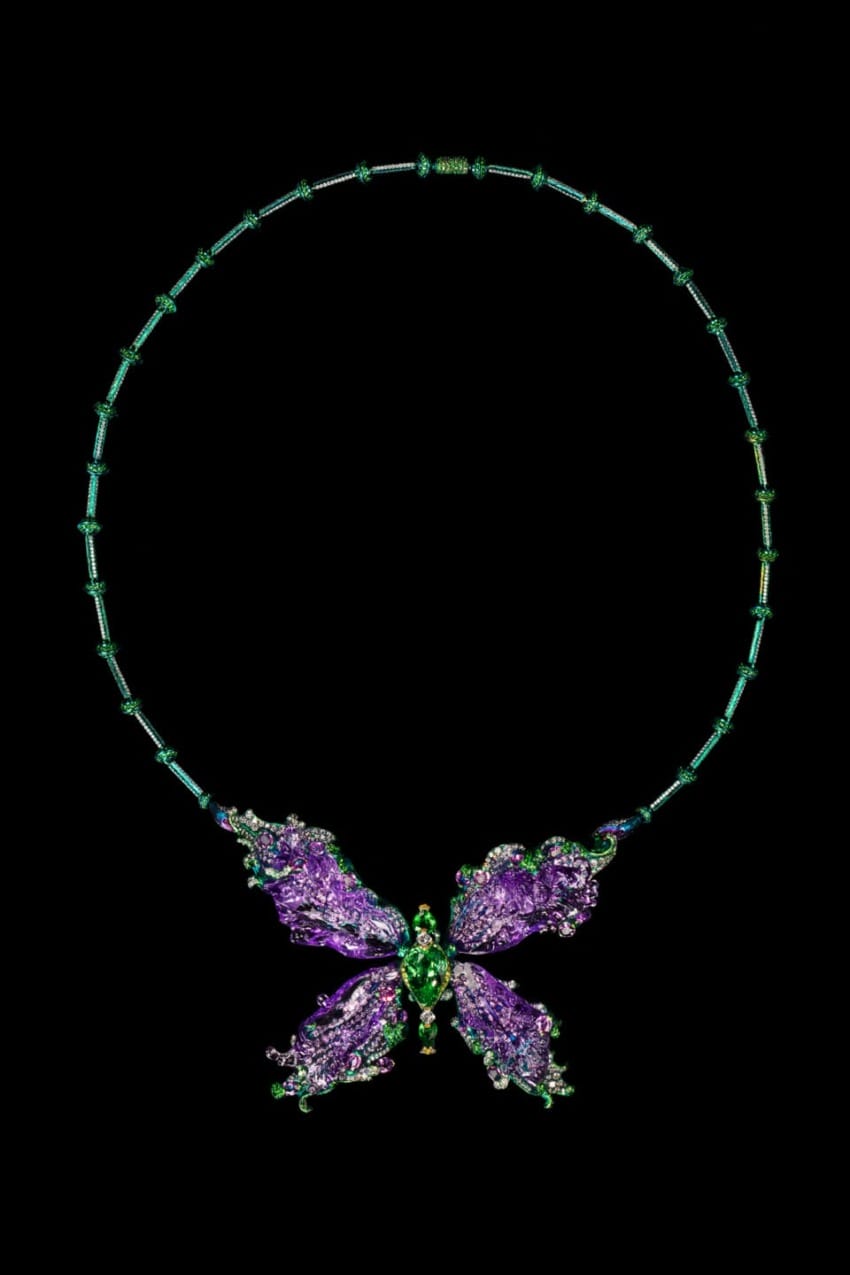 A butterfly-shaped necklace with purple and green gemstones on a black background.
