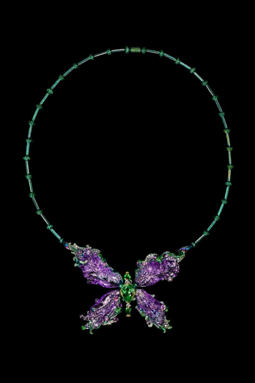 A butterfly-shaped necklace with purple and green gemstones on a black background.