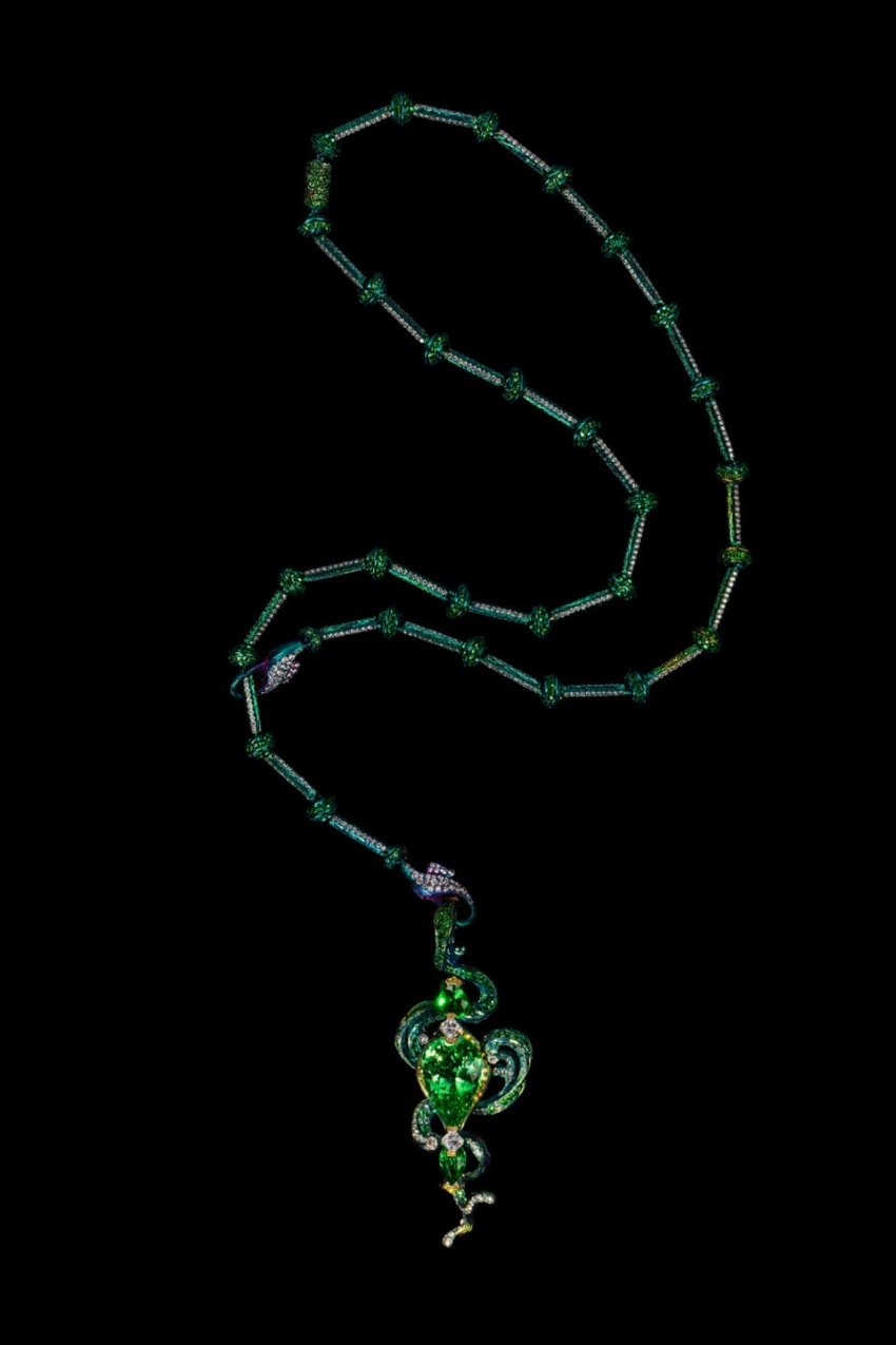 Green beaded necklace with intricate pendant featuring swirling patterns on a black background.