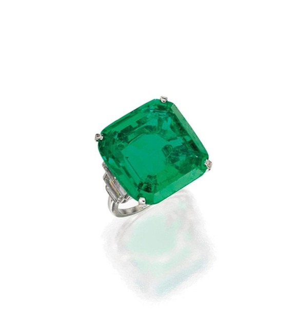 Emerald-cut green gemstone ring with silver band on a reflective surface.
