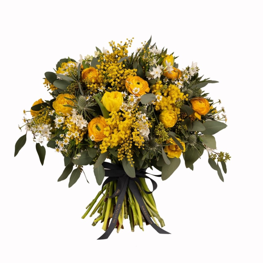A bouquet of yellow and white flowers with green leaves, wrapped with a black ribbon.