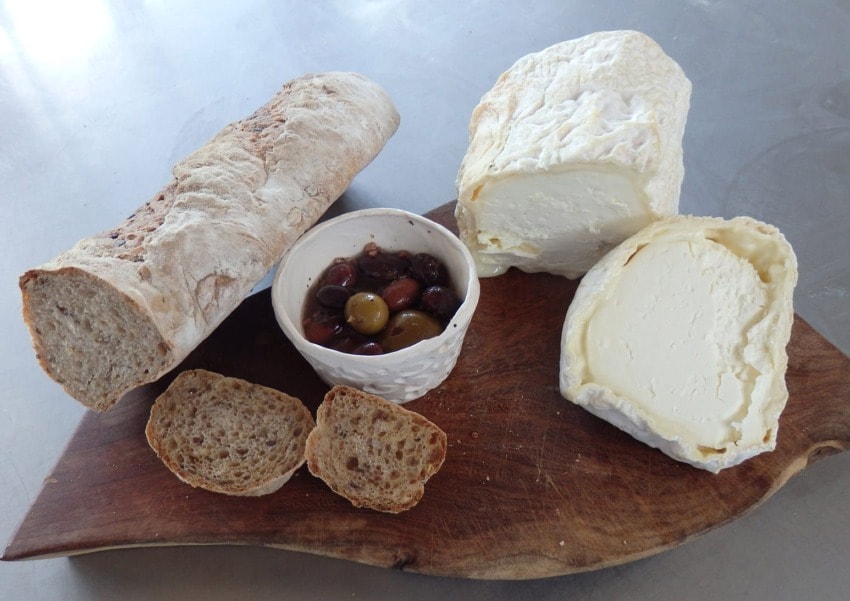 Rustic bread, a bowl of mixed olives, and creamy cheese on a wooden board.