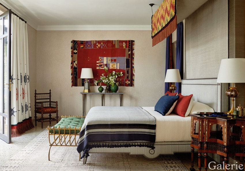 Modern bedroom with a neatly made bed, decorative pillows, tapestry on the wall, and elegant wooden furniture.