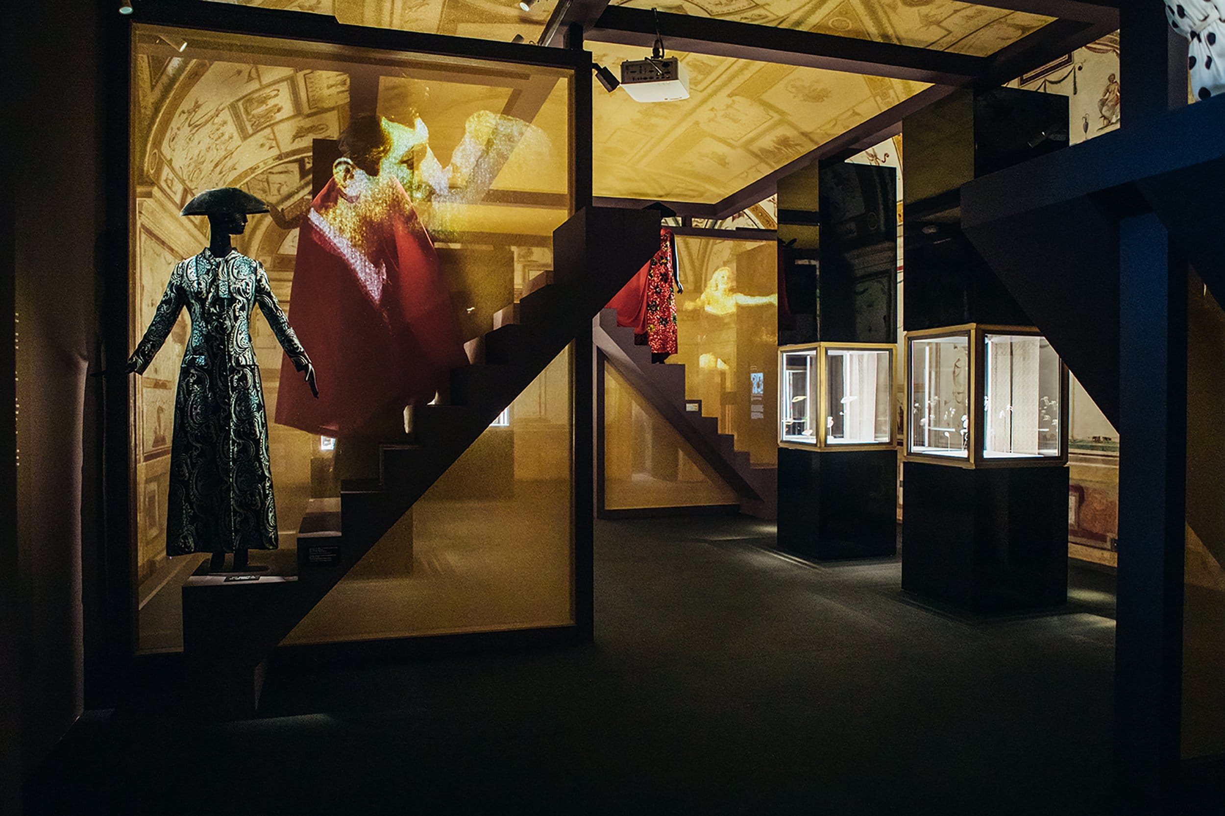 Exhibit room with historical costumes displayed, dimly lit atmosphere highlighting intricate designs and glass display cases.