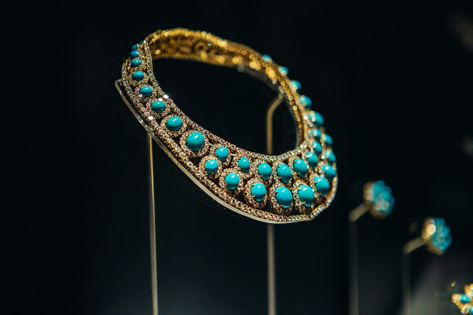 Gold necklace adorned with blue gemstones displayed on stand against dark background.