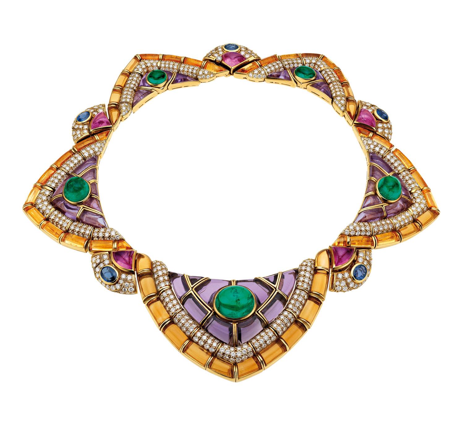 Colorful geometric necklace with gemstones, including emeralds and rubies, set in a gold design with purple accents.