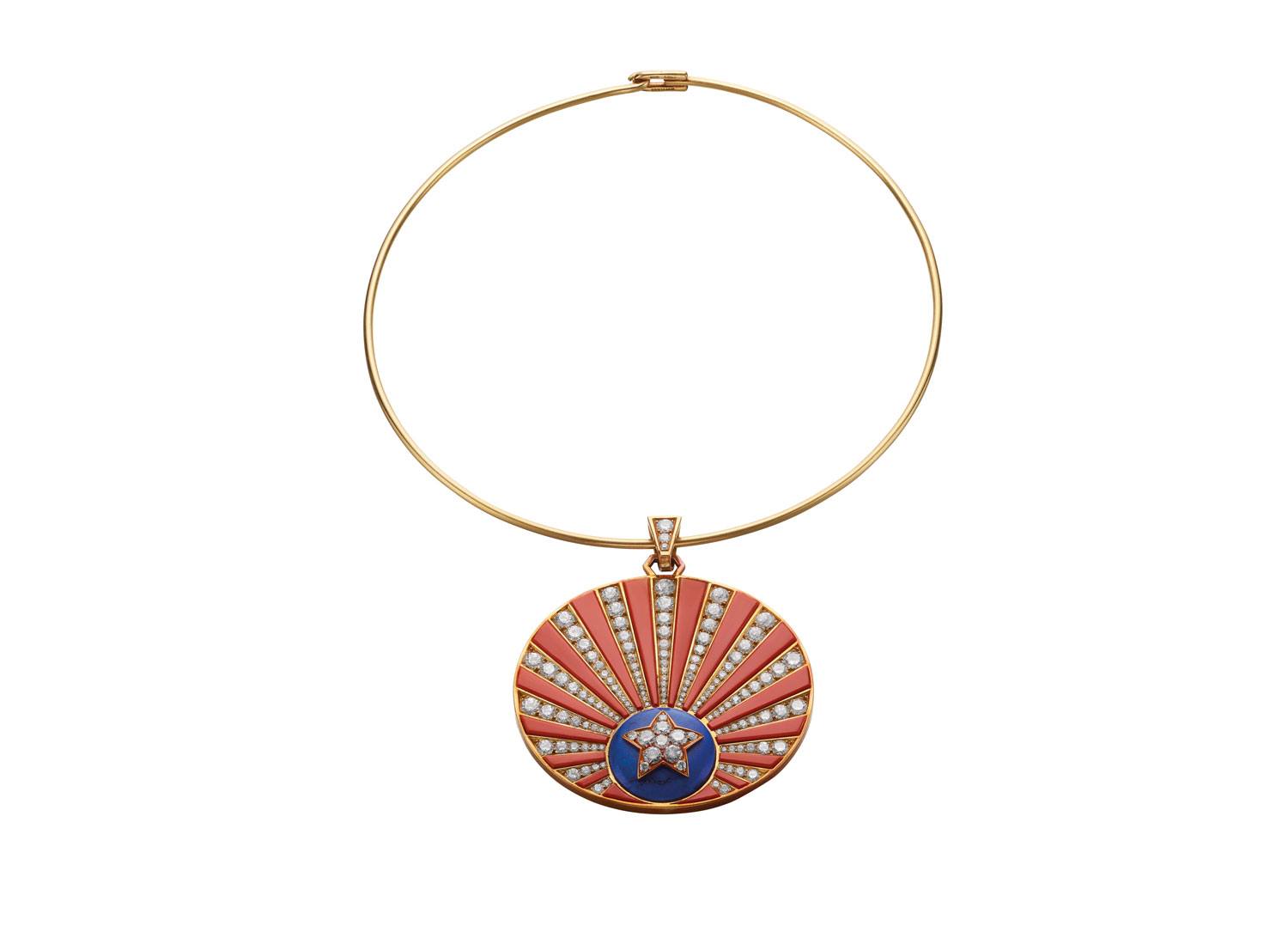 Gold necklace with a round pendant featuring a sunburst design in red and blue with embedded sparkling stones.