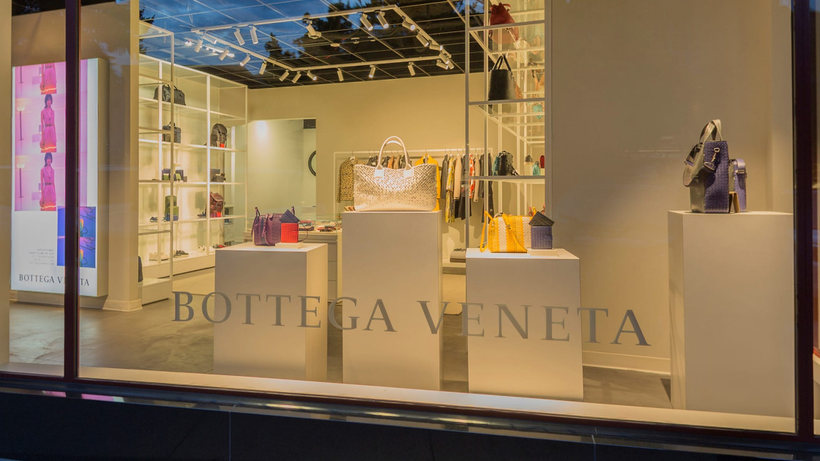 Storefront display featuring luxury handbags on pedestals inside a Bottega Veneta boutique.