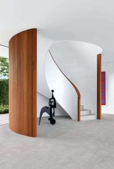Modern spiral staircase with wooden accents and abstract sculpture displayed at the base in a minimalist interior.