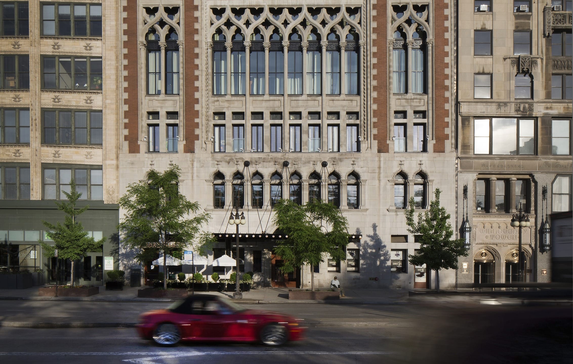 Historic building facade with ornate windows and a red convertible driving by on the street in front.
