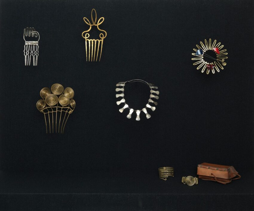 Assorted decorative hair combs, a necklace, and a bracelet displayed on a black background with a small brown bag.