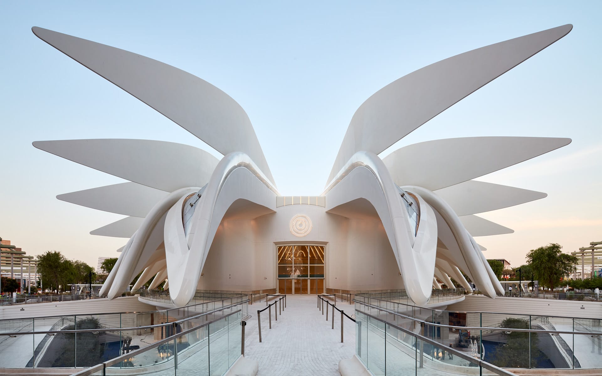 Modern architectural building with large, sweeping white arches and glass entrance, set against a clear blue sky.