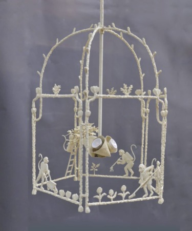 Intricate ivory-colored decorative structure with monkey figures and floral patterns against a gray background.