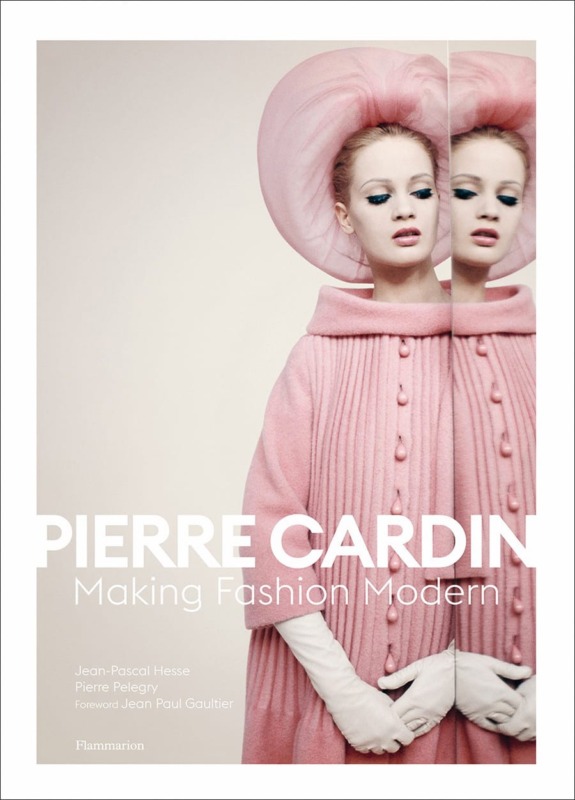 Cover of the book "Pierre Cardin: Making Fashion Modern" with a model in a pink coat and hat standing by a mirror.