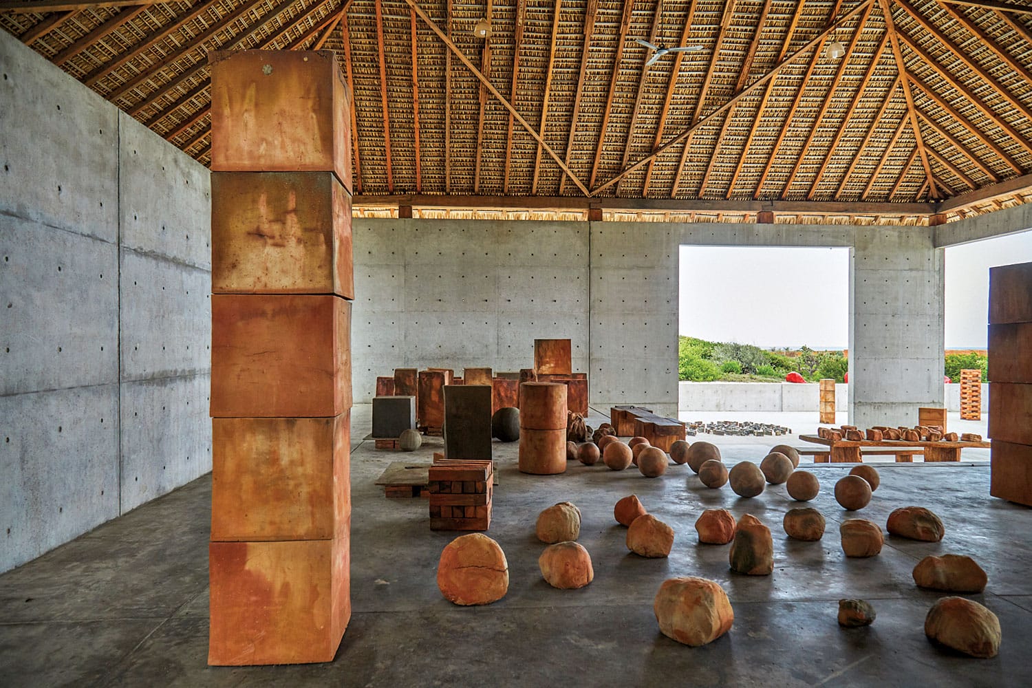 Indoor art installation with stacked and scattered geometric shapes in a spacious room with concrete walls and wooden ceiling.