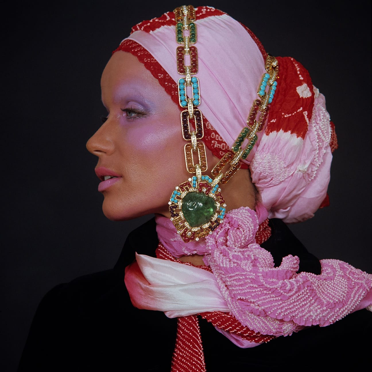 Woman in vibrant headscarf and jewelry, side profile, with elaborate beadwork and accessories against dark background.