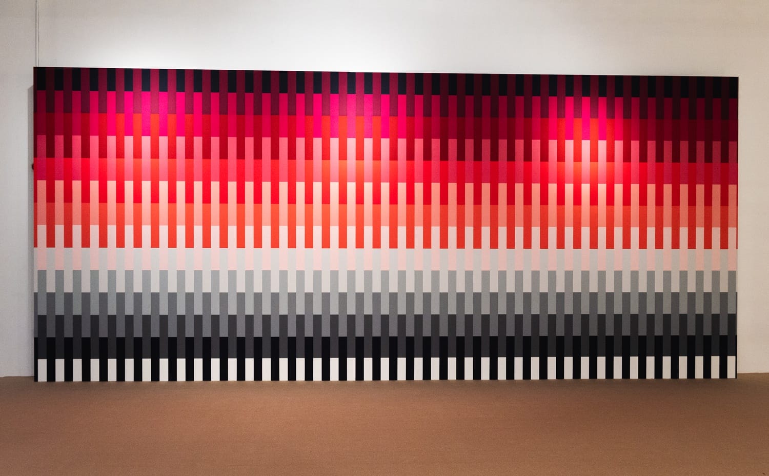 Vibrant wall art installation featuring vertical bars in a gradient from red to black against a plain interior backdrop.