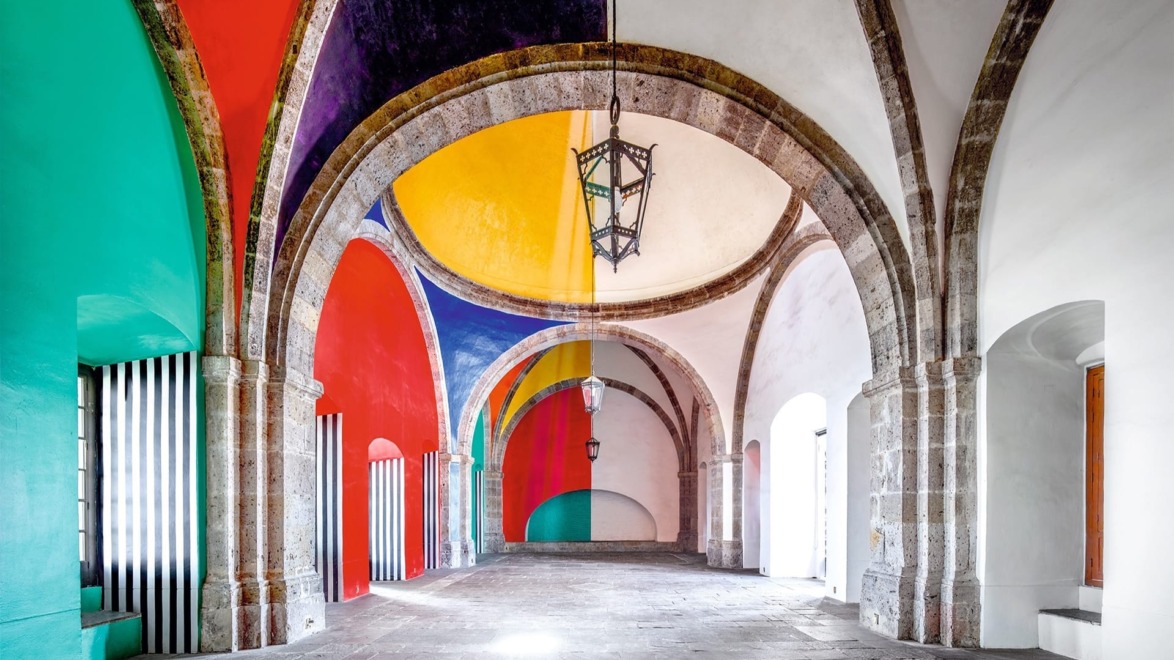 Colorful arched hallway with vibrant geometric patterns on walls and ceiling, featuring stone floor and hanging lantern.
