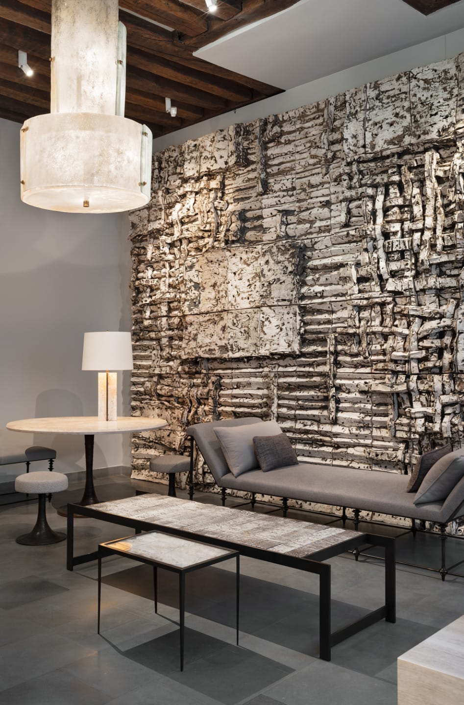 Modern living room with textured wall, contemporary furniture, nested tables, gray sofa, and unique lighting fixtures.
