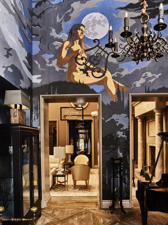 Elegant interior with a grand chandelier, artistic ceiling mural, cozy seating area, and a piano in a luxurious setting.