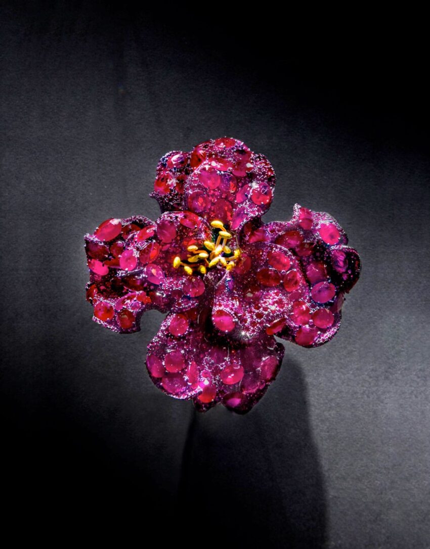 Vibrant red glass flower with yellow stamens on dark background, showcasing intricate petal details and artistic craftsmanship.