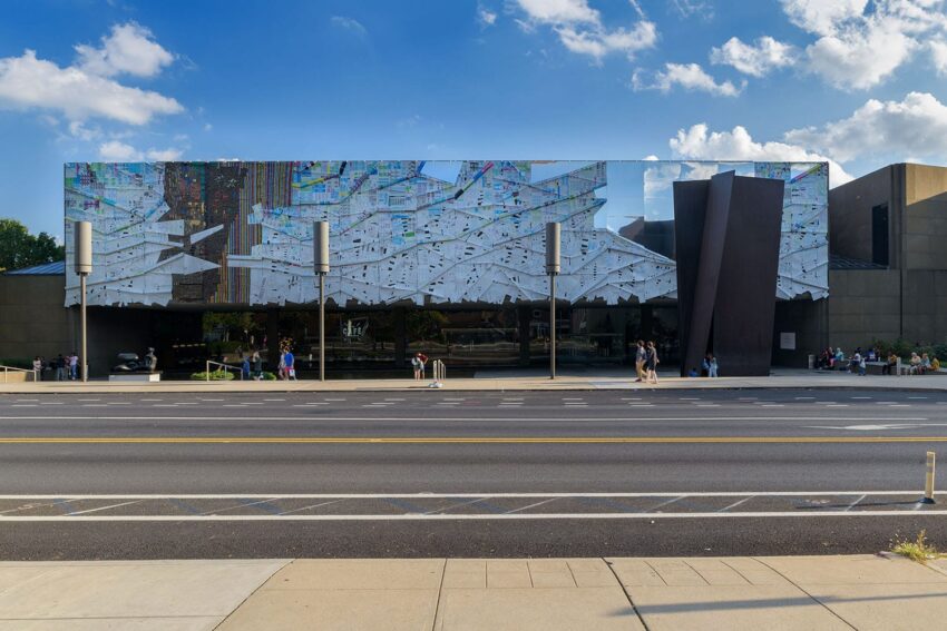 Exterior view of a modern art museum with mirrored facade reflecting the sky, people walking nearby on a sunny day.