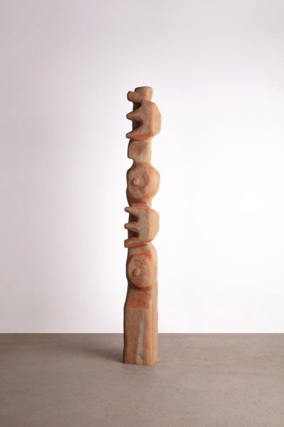 Tall wooden totem sculpture with abstract carvings on a plain background.