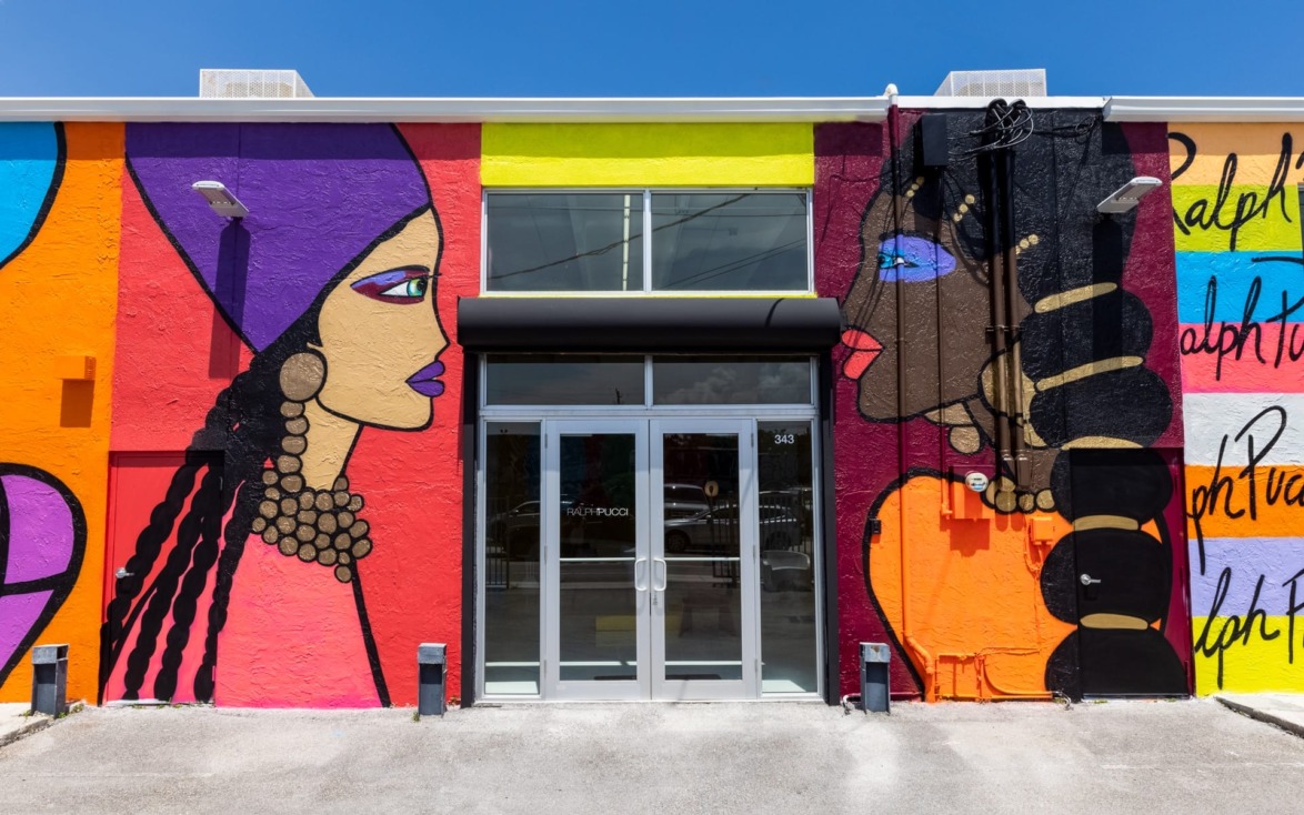 Colorful mural on building exterior featuring two stylized female faces with vibrant patterns and bold jewelry designs.