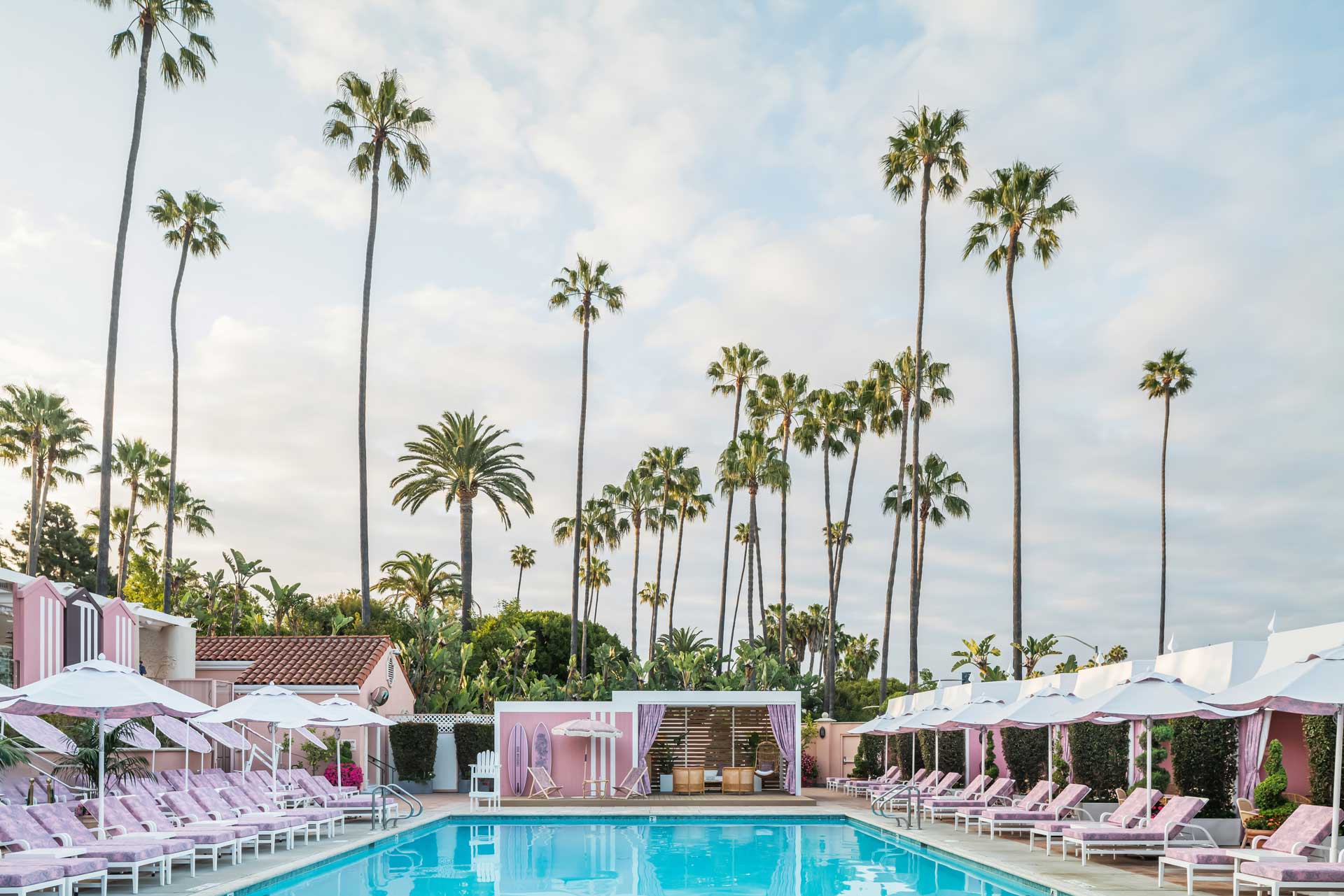 Luxury hotel poolside with pink cabanas, palm trees, and a clear blue sky, creating a relaxing and tropical atmosphere.