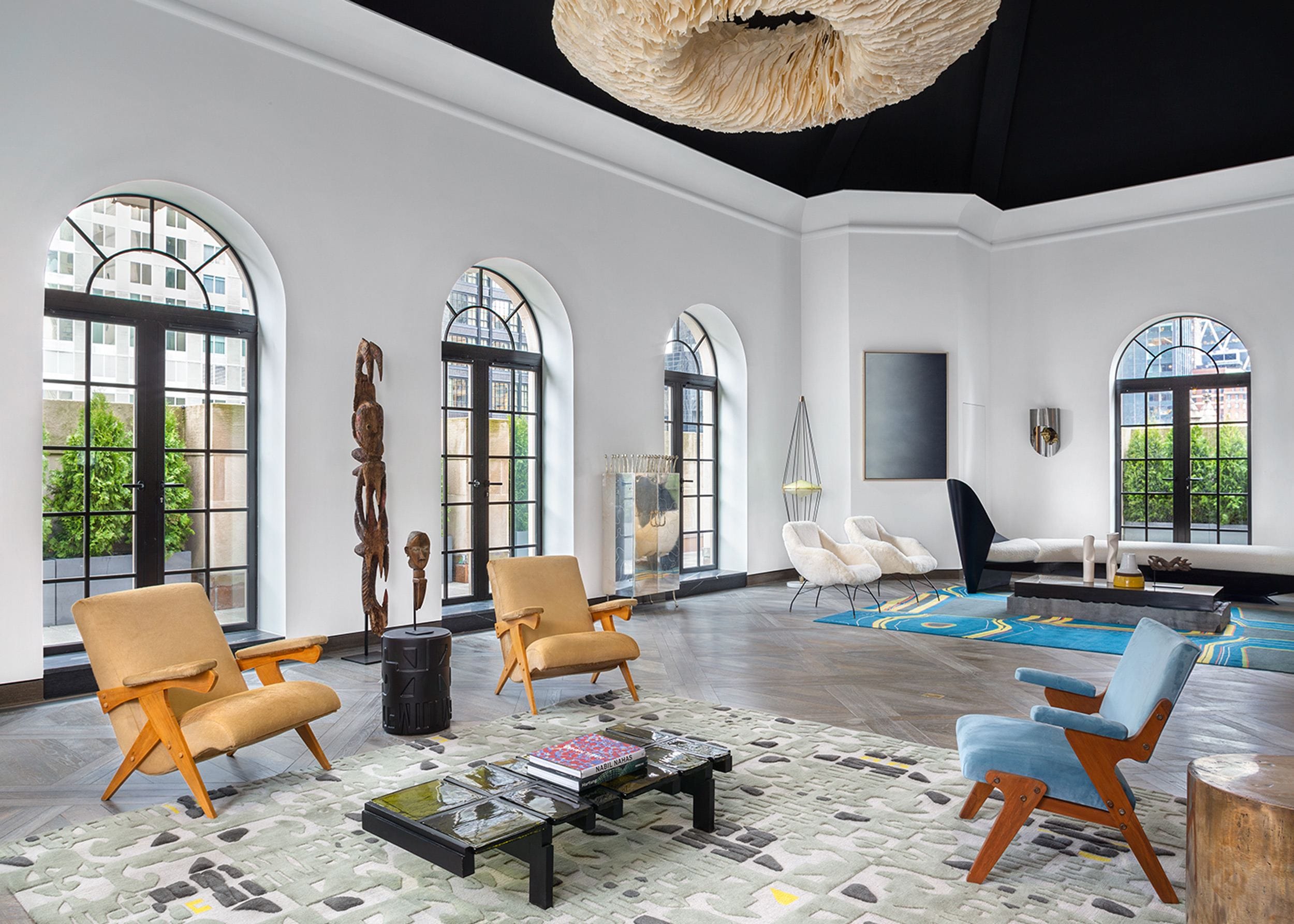 Modern living room with arched windows, stylish furniture, abstract rug, and unique ceiling fixture.